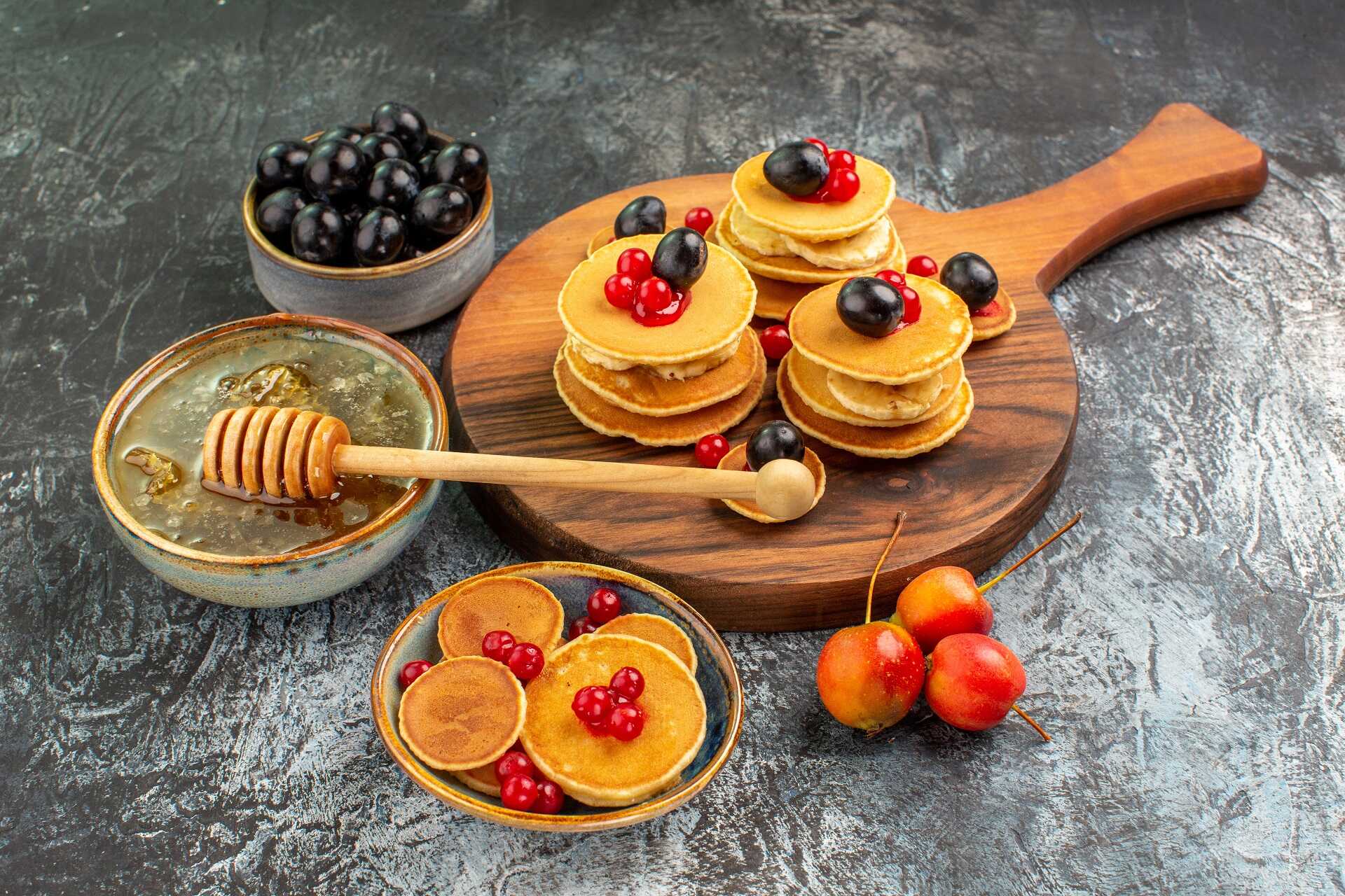 close-up-view-of-classic-pancakes-on-cutting-board-honey-and-fruits_optimized